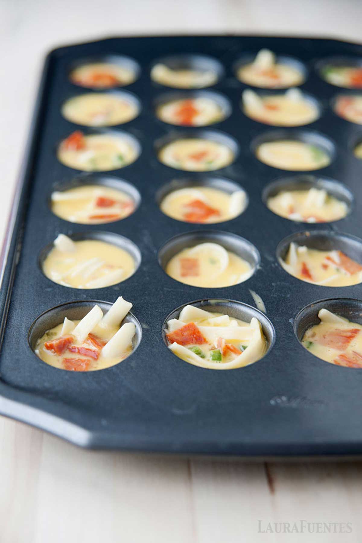 un molde para minimuffins con mezcla de huevo, leche y toppings