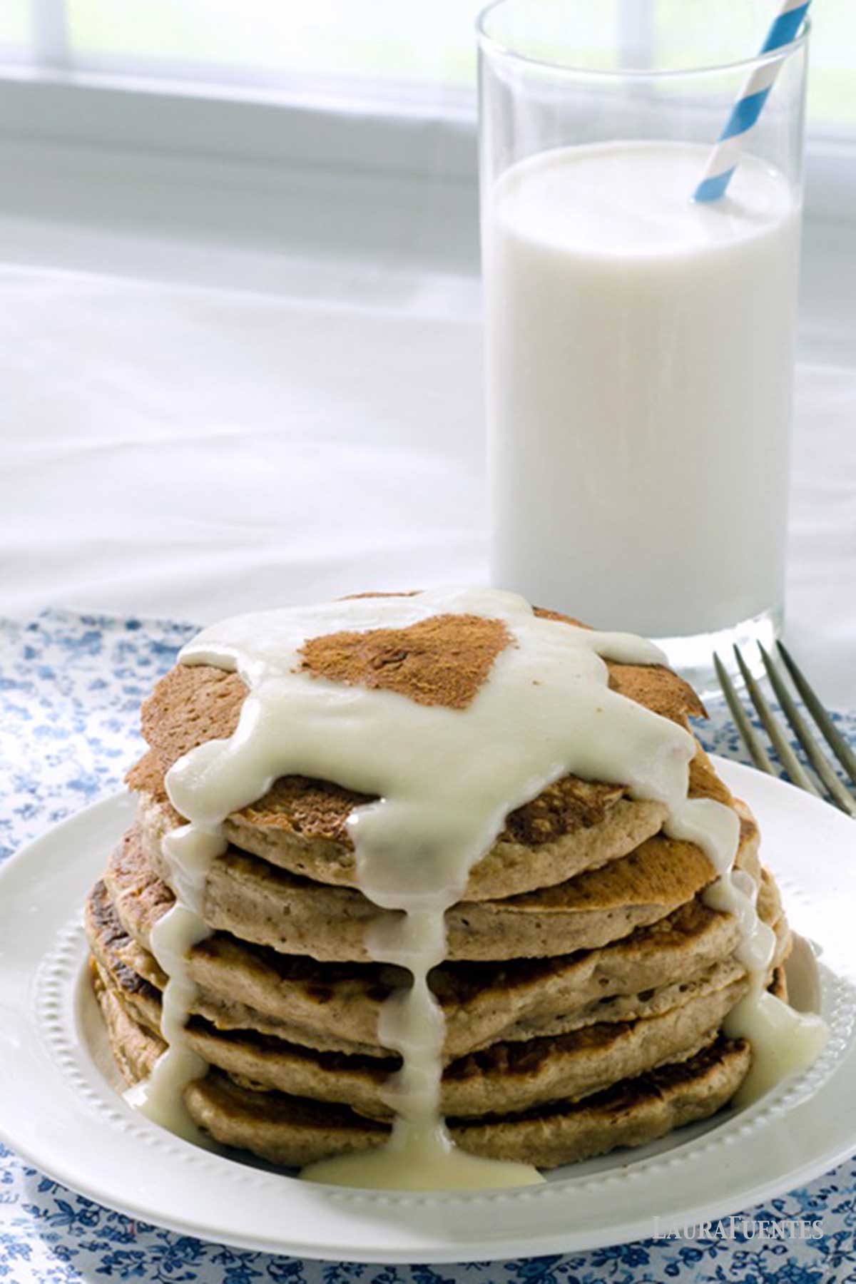 una pila de pancakes de canela con glaseaso sobre un plato, con un vaso de leche detrás.
