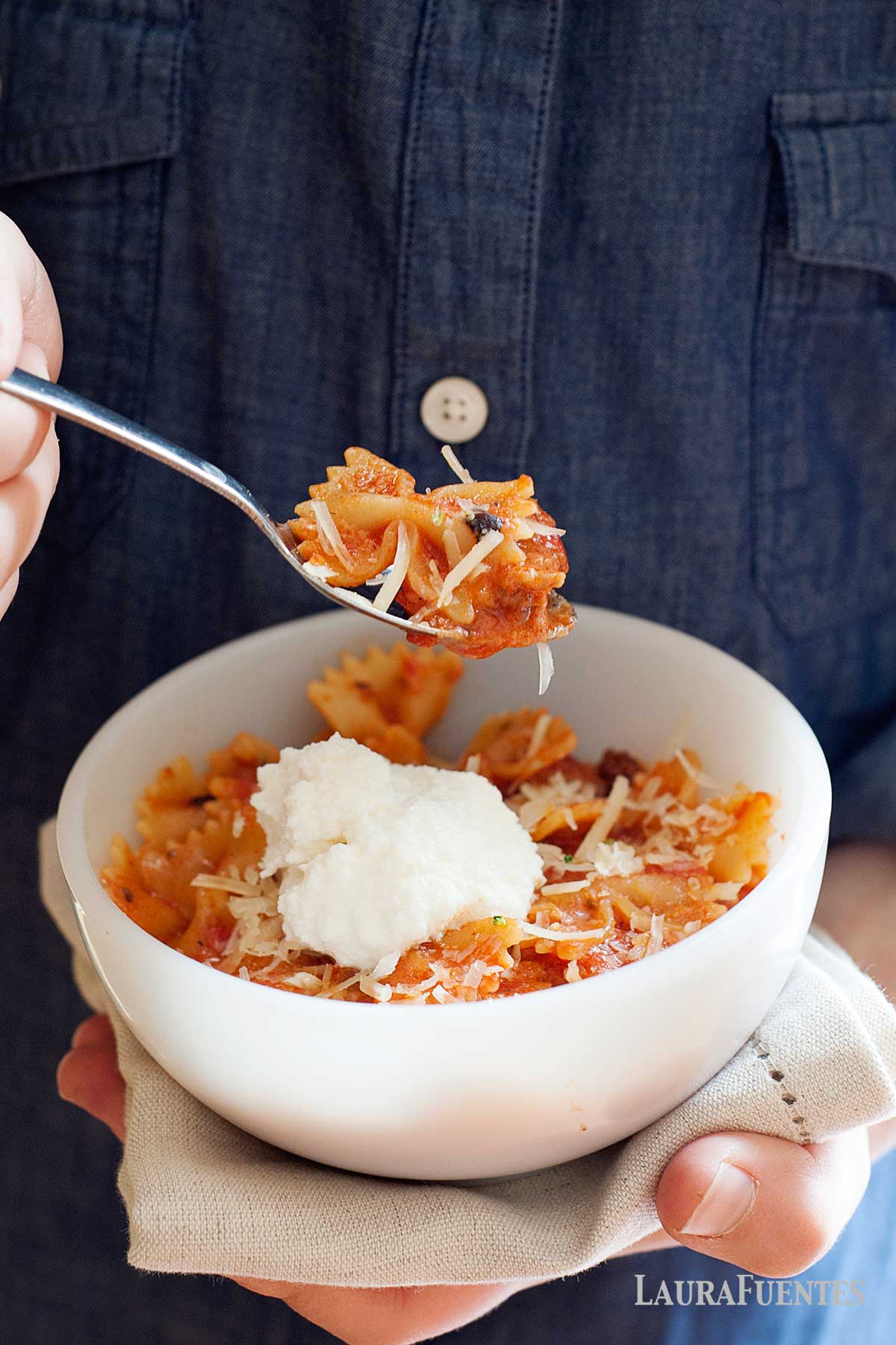 una persona sosteniendo un tazón y un tenedor con pasta con carne molida y salsa de tomate
