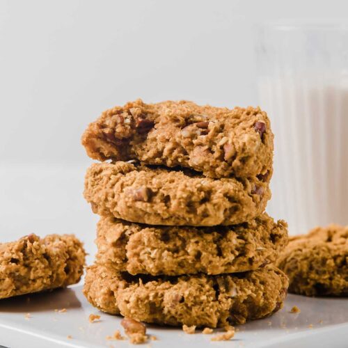 una pila de galletas de calabaza y un vaso de leche detrás