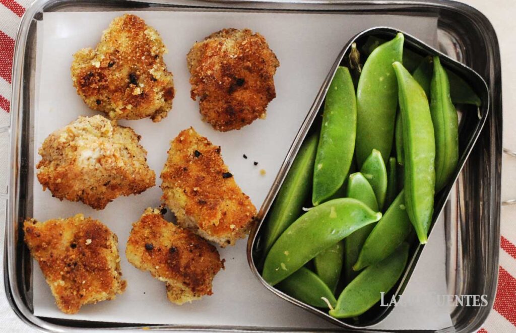una lonchera con seis nuggets de pollo y un contenedor más pequeño con judías verdes
