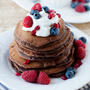 una pila de tortitas de chocolate con crema y frutos rojos encima