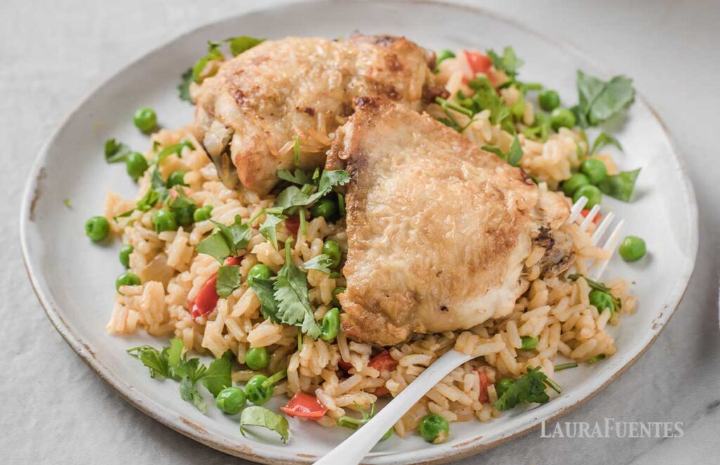 un plato con arroz con contramuslos de pollo y guisantes