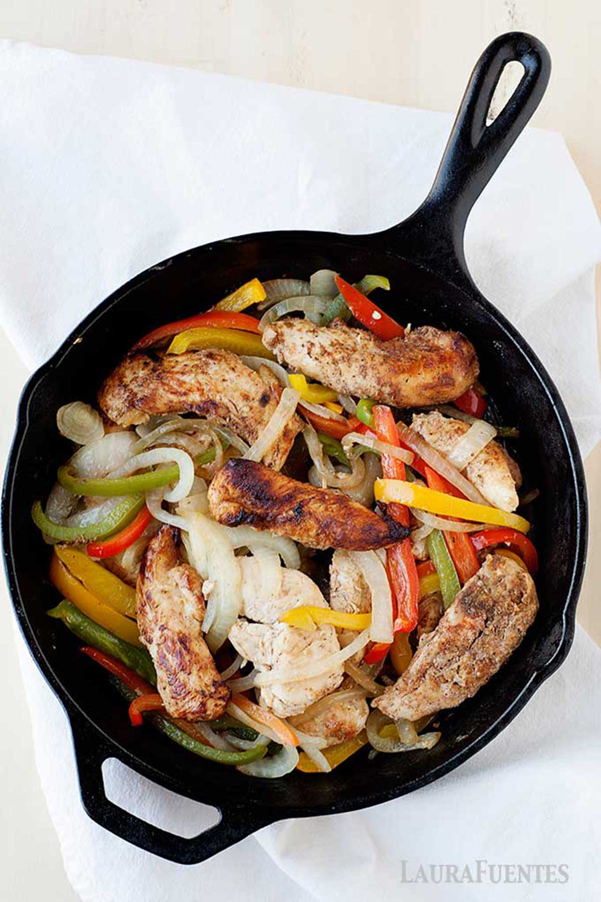 Pollo con pimientos y cebolla en una sartén de hierro.