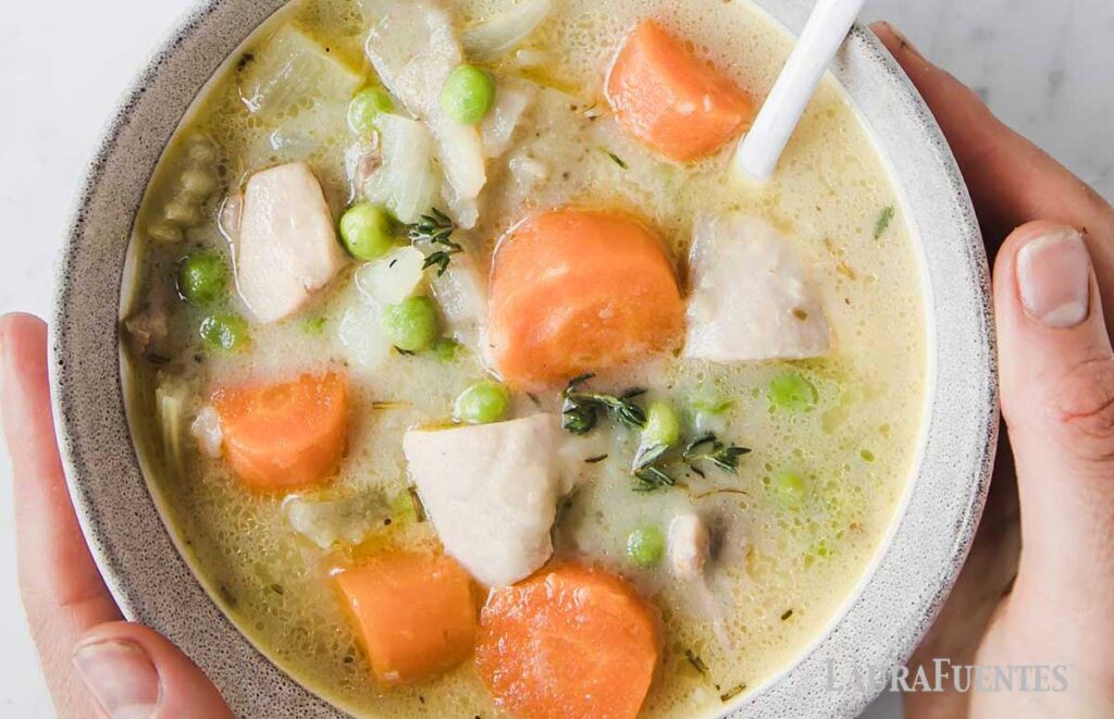 una persona sosteniendo un cuenco con guiso de pollo, patatas y verduras
