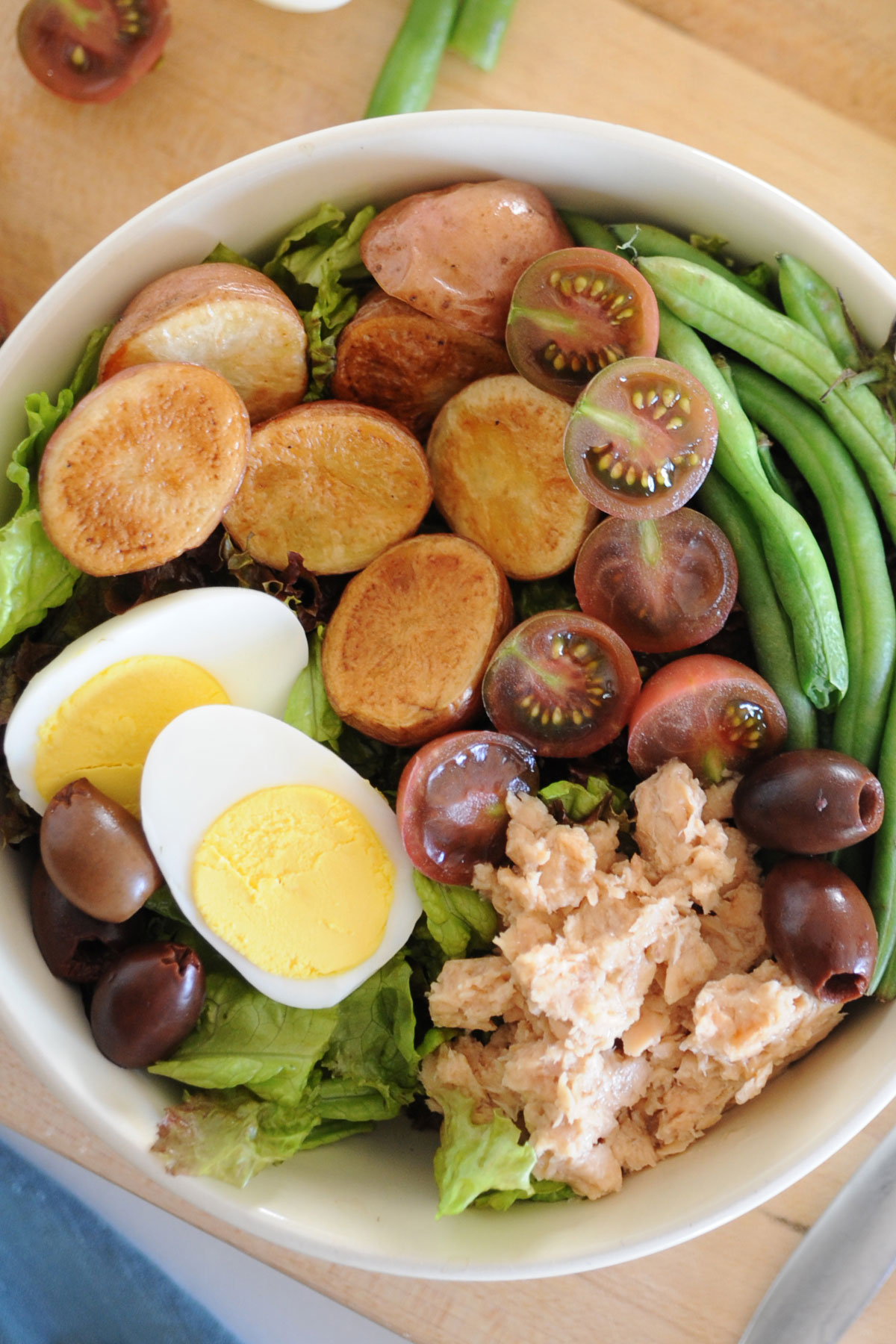 ensalada nicoise con tomates, aceitunas, judias verdes, salmón, y lechuga en un bol