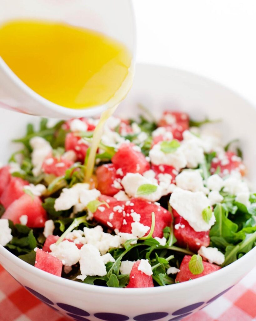 bol de ensalada de sandía, menta y queso siendo rociado con vinagreta de naranja