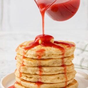 sirope de fresa siendo vertido sobre una pila de tortitas