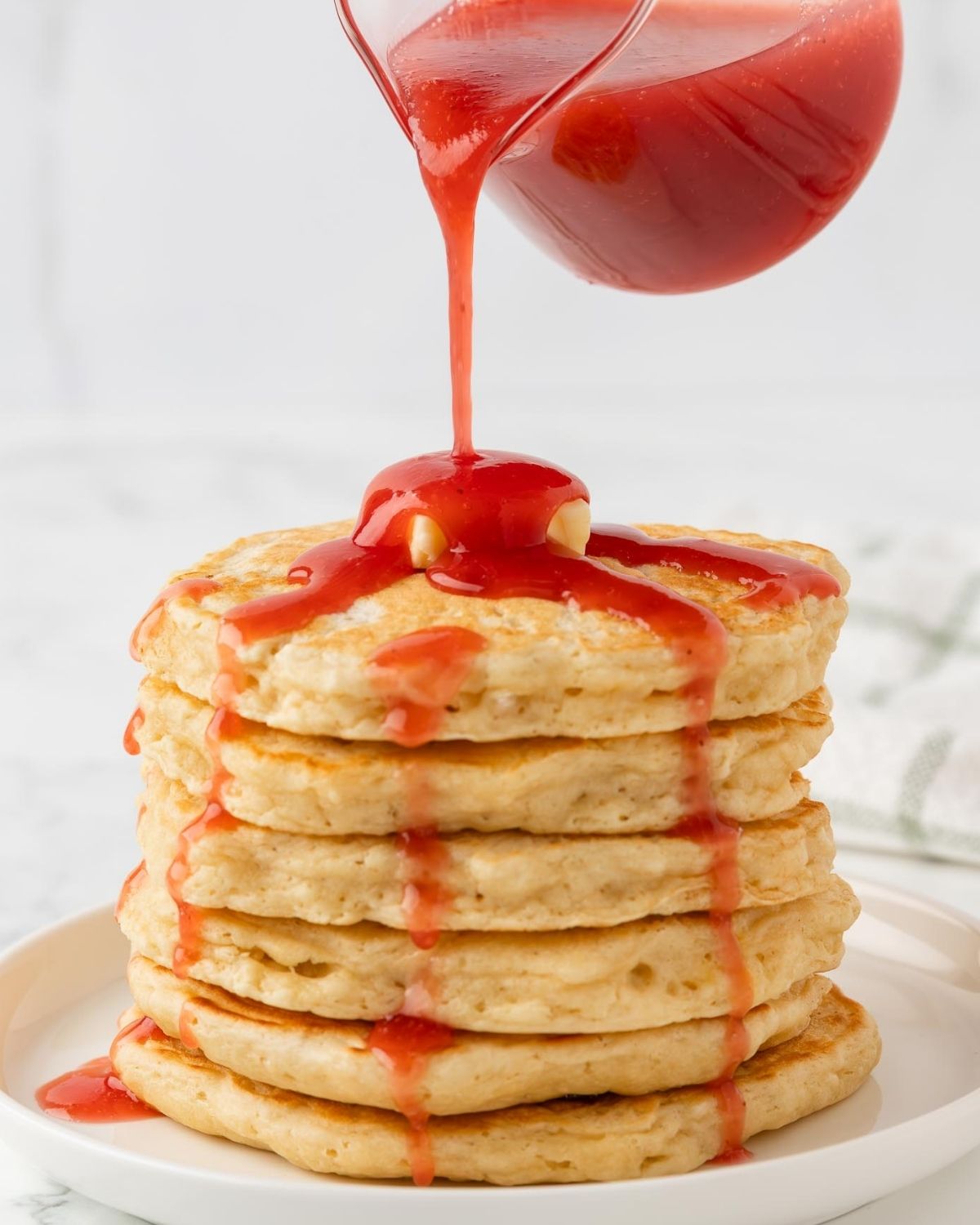 sirope de fresa siendo vertido sobre una pila de tortitas