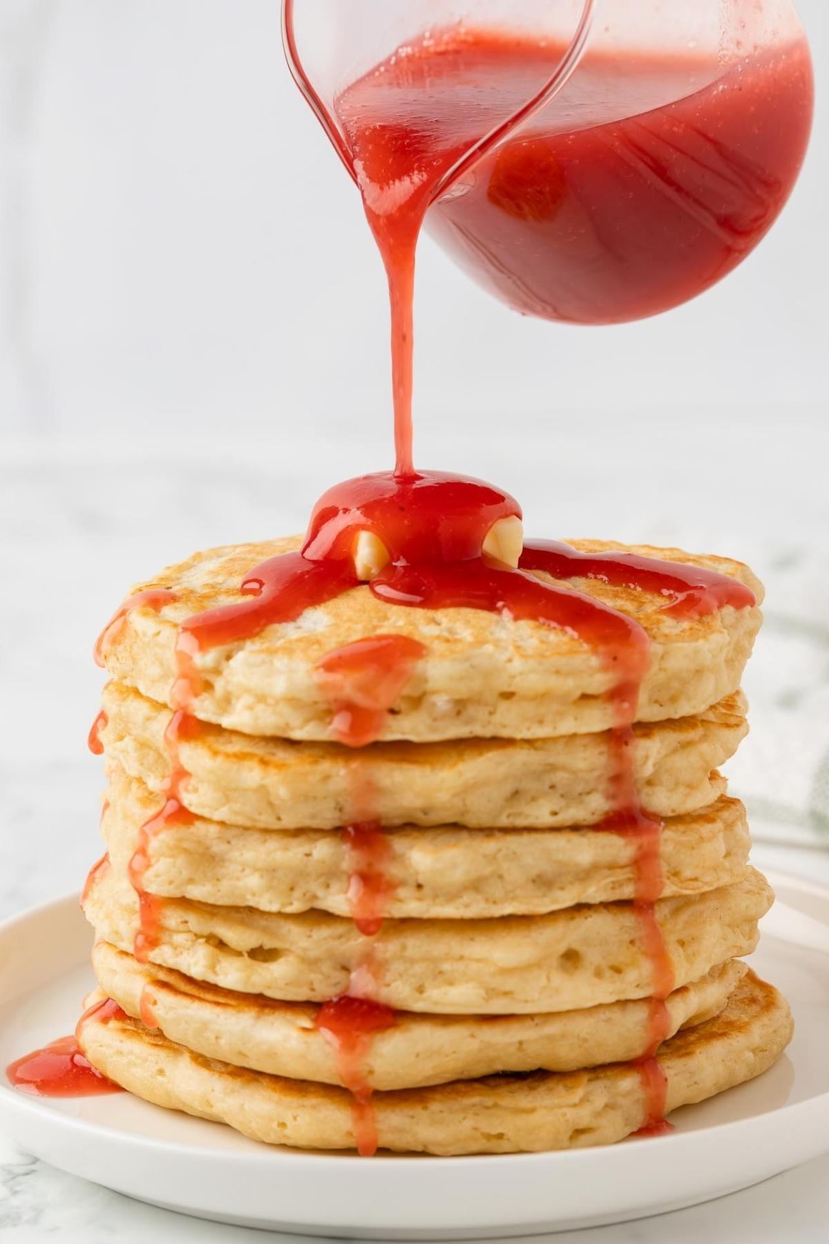 sirope de fresa siendo vertido sobre una pila de tortitas