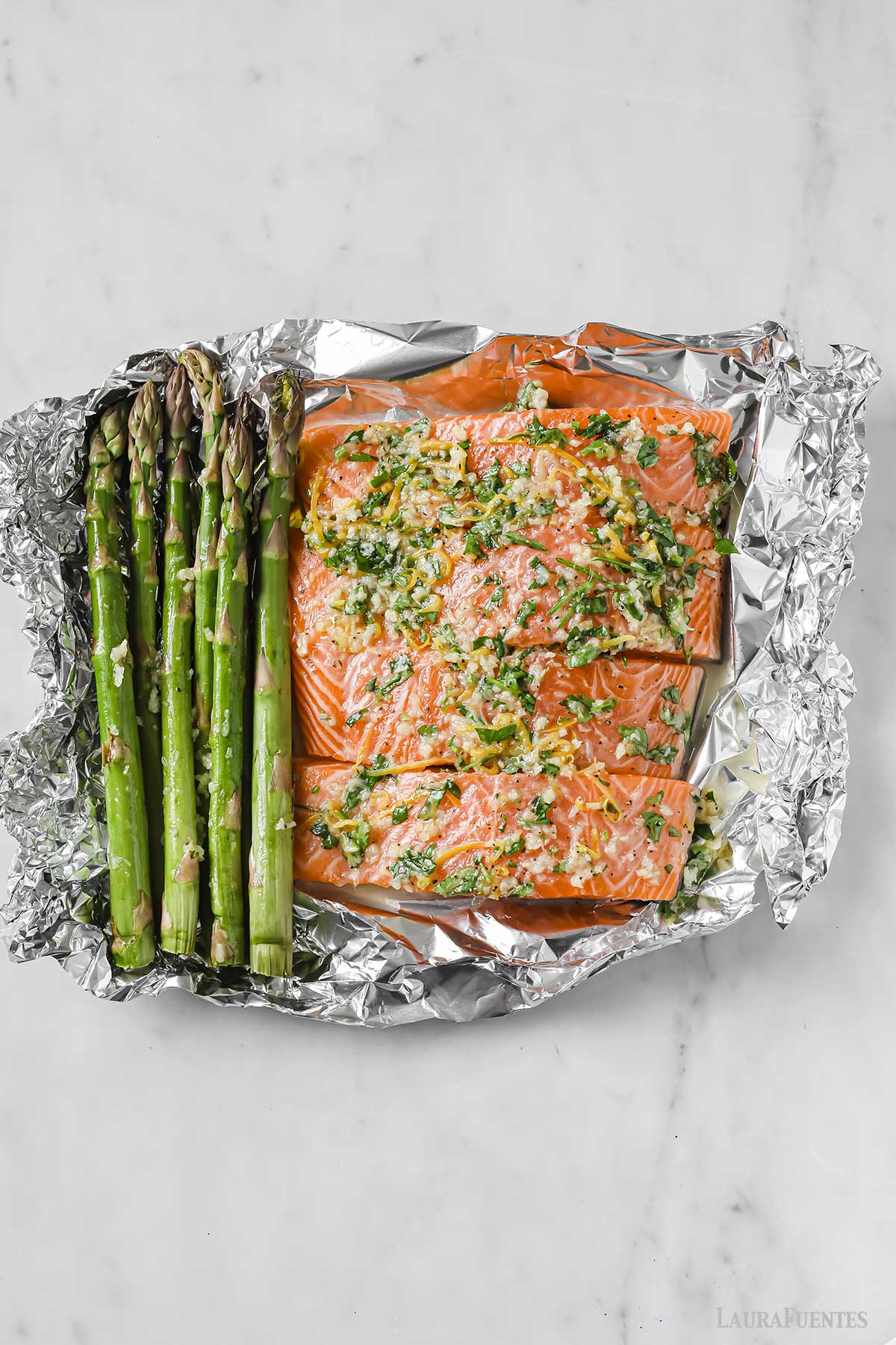 Salmón y espárragos sazonados y crudos sobre papel aluminio.