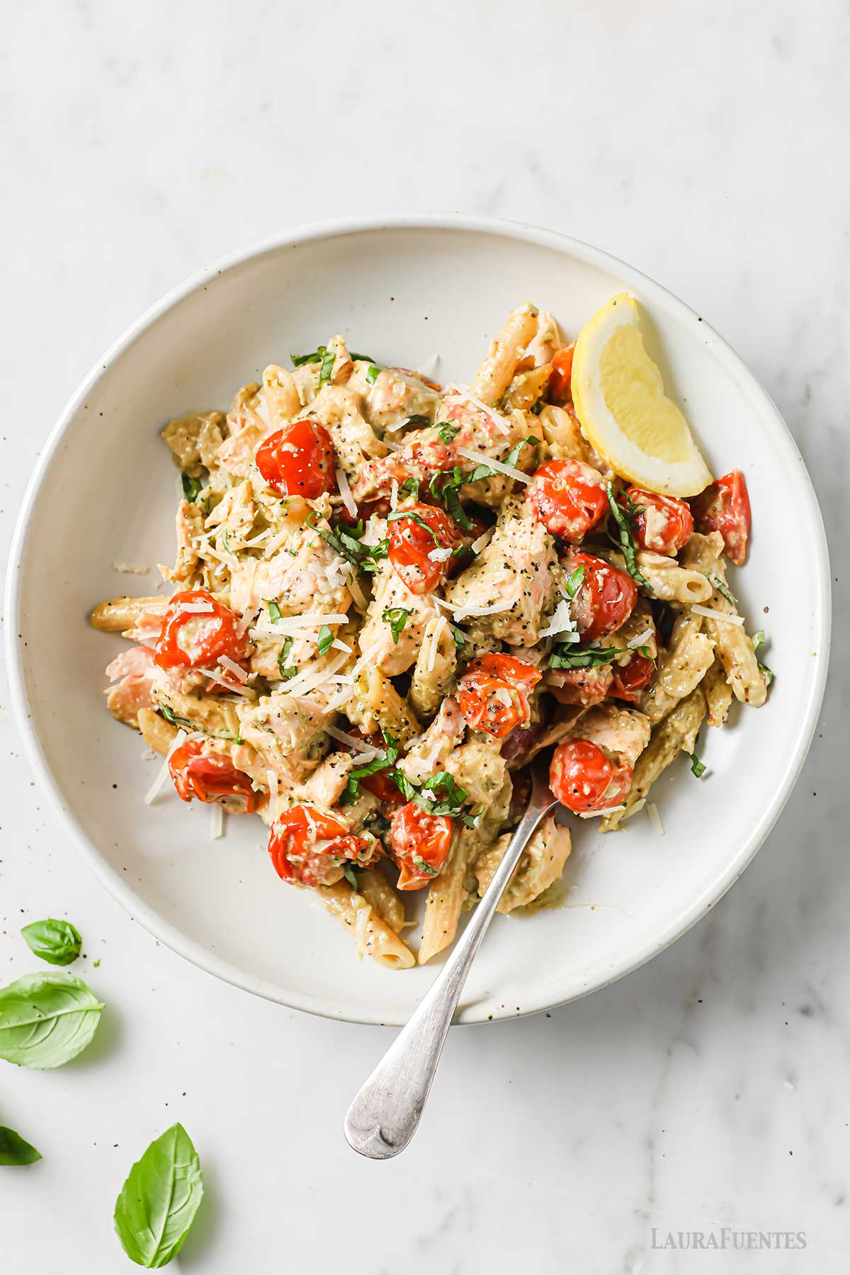 Plato de Pasta con Salmón, un tenedor, un gajo de limón y hojas de albahaca.
