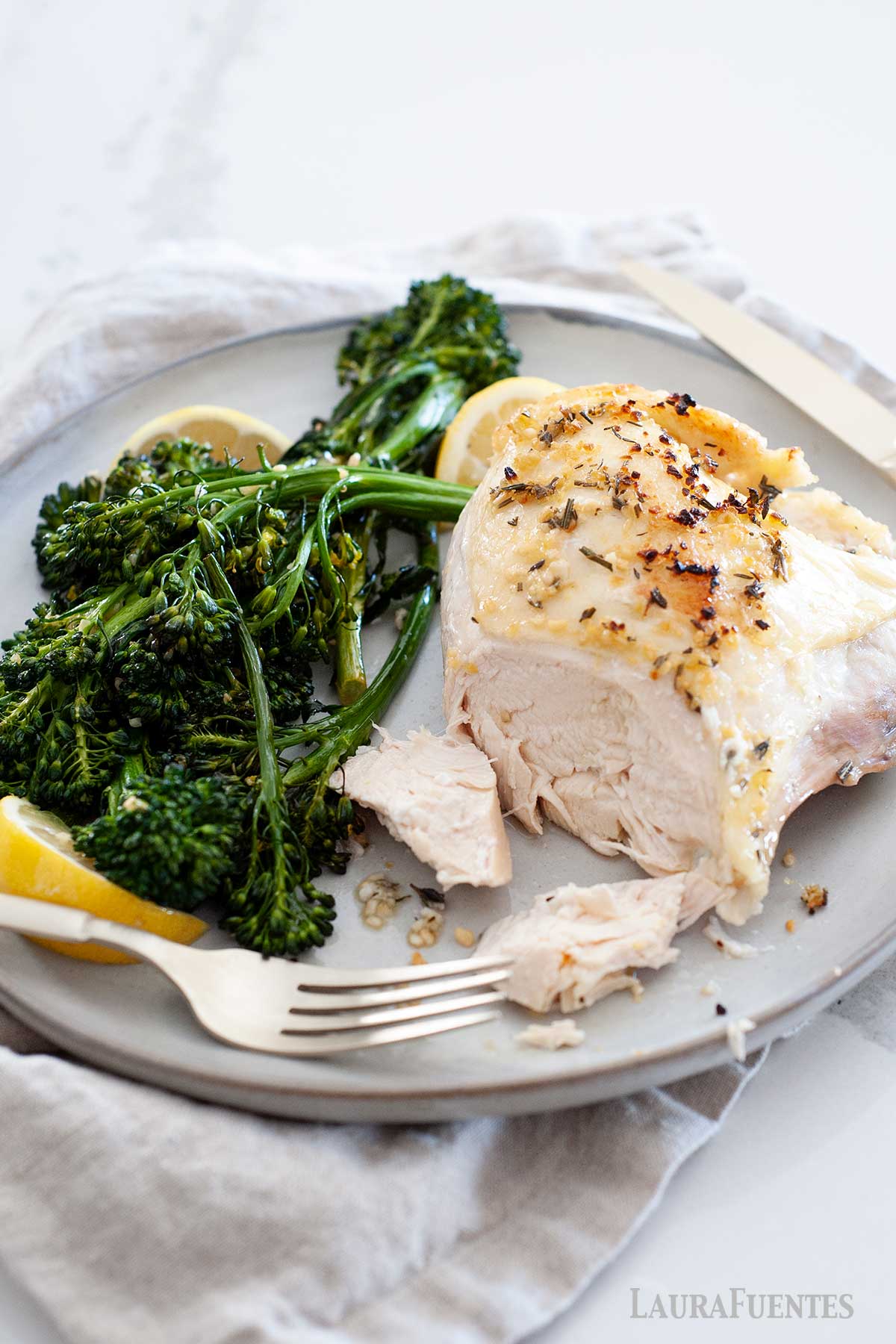 Pechuga de Pollo con Hueso al horno servida en un plato con brocolini y rodajas de limón.