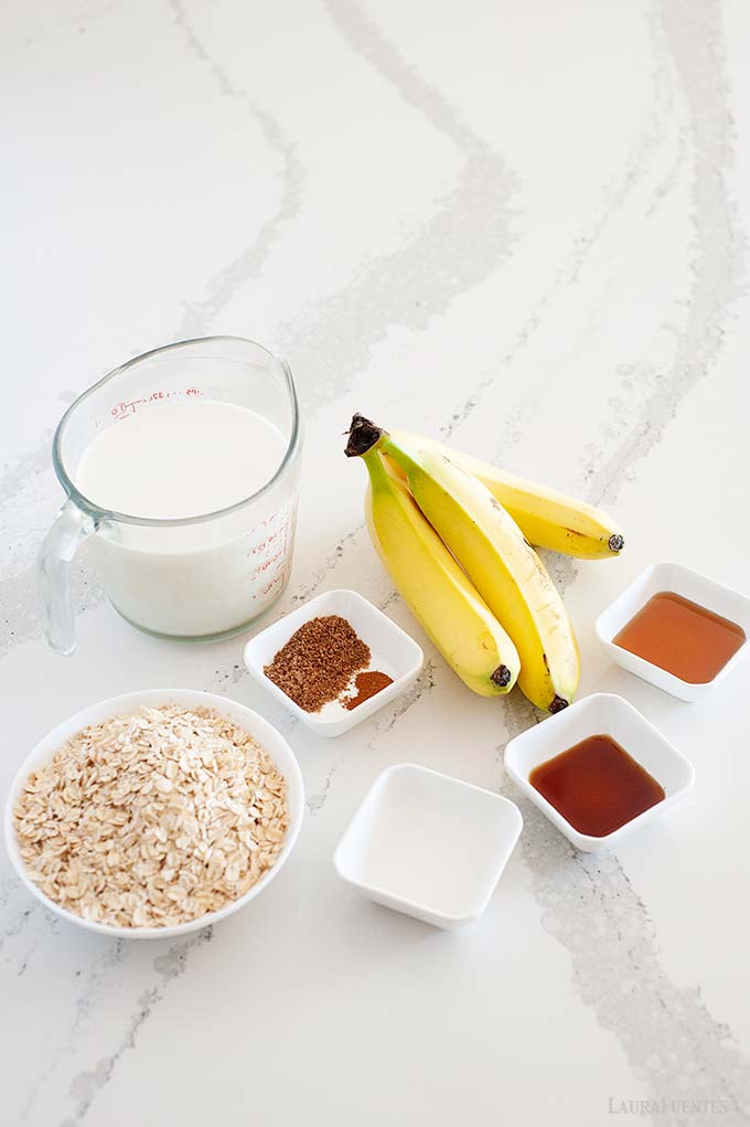 tres plátanos, una jarra de leche, un tazón de avena cruda, sirope de arce, extracto de vainilla, linaza y canela