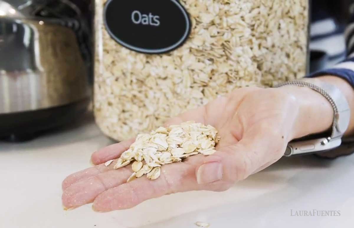 una mano mostrando un puñado de avena arrollada, detrás, un frasco con avena