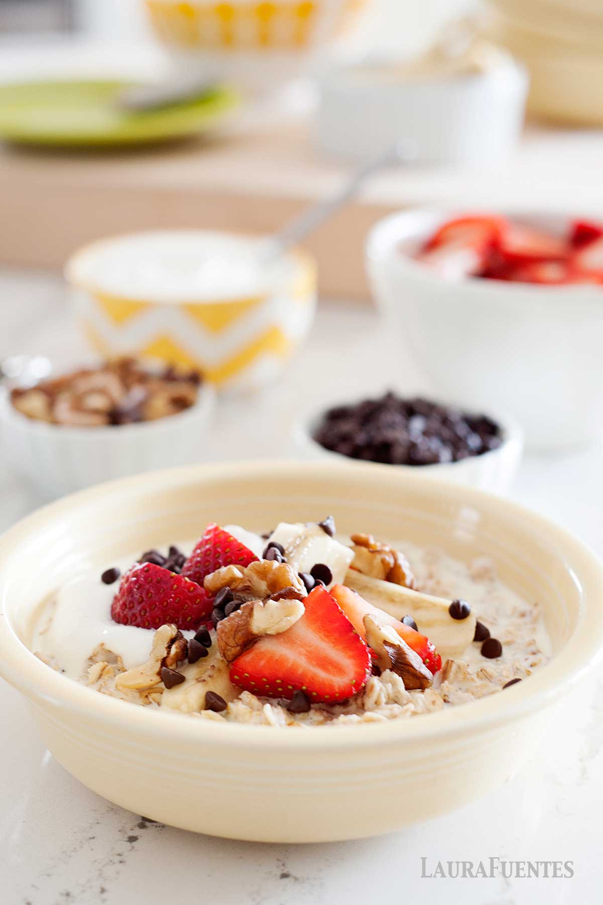 bowl de avena con frutos rojos, junto a otros bowl con chips de chocolate, fresas y nueces