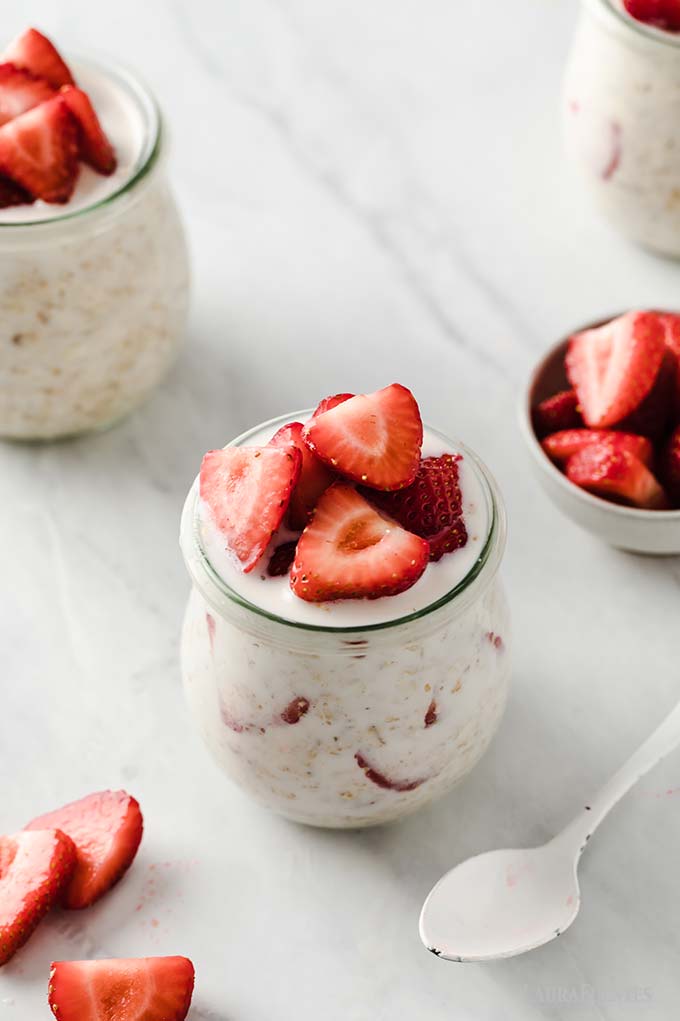 un frasco de avena con fresas, una cuchara y trozos de fresas