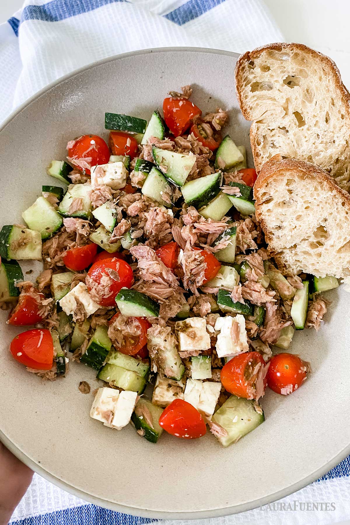 un plato con ensalada de atún, tomate y pepino, con dos trozos de pan