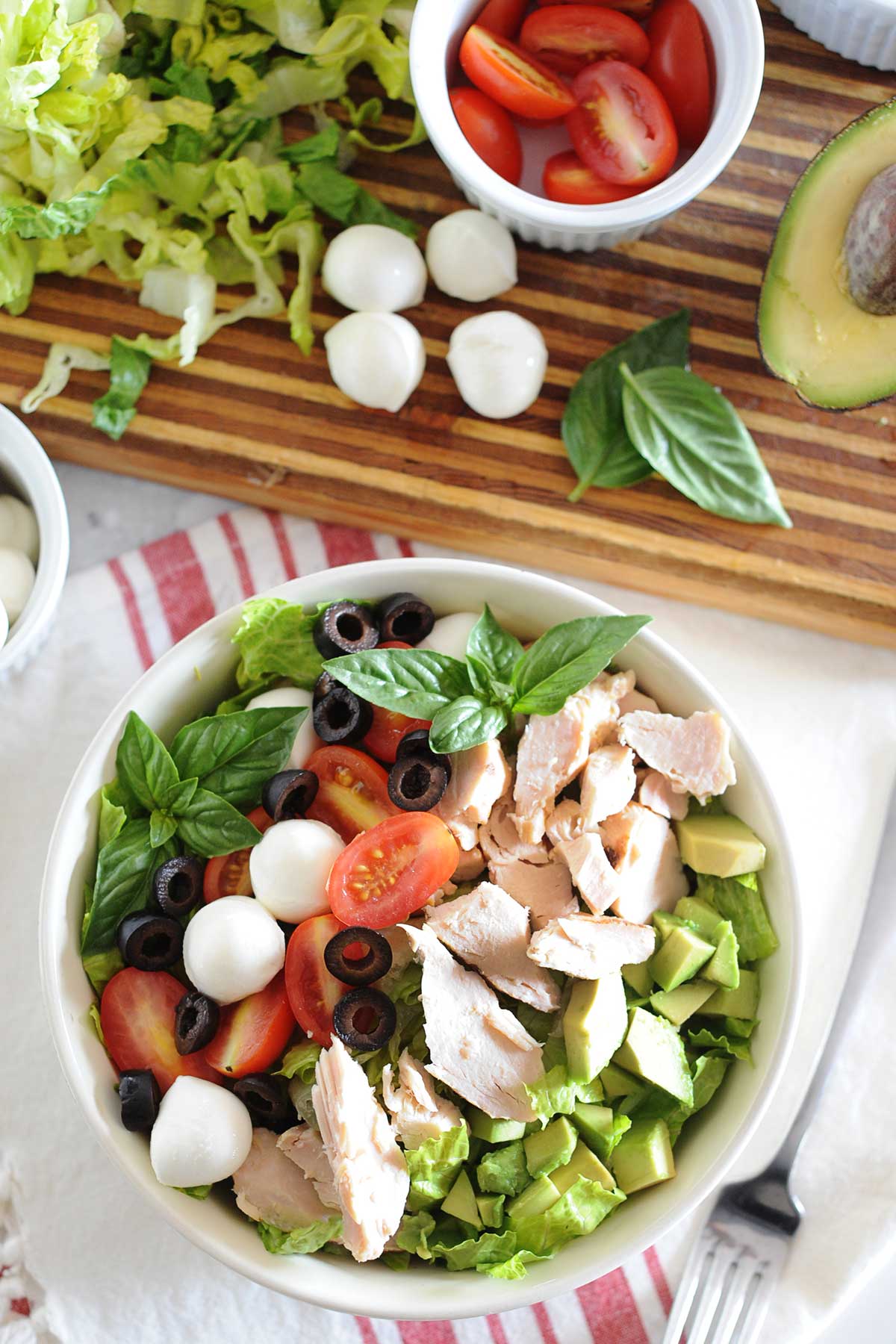 un bol de ensalada caprese con pollo, aguacate, tomate, albahaca, mozzarella, lechuga y aceitunas