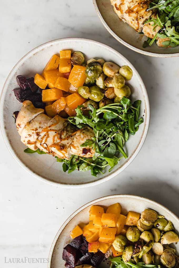 un plato con pollo, verduras asadas y hojas verdes