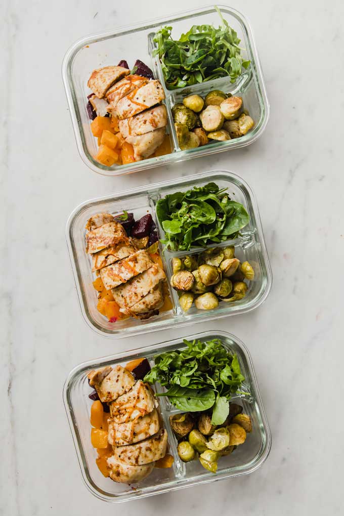 tres recipientes con verduras asadas, pollo y hojas verdes.