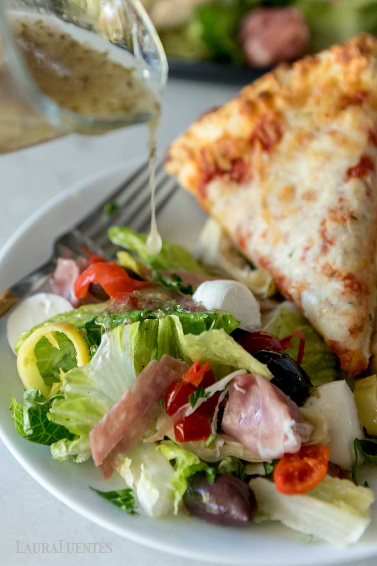 un plato con una porción de pizza y ensalada antipasto con aderezo.