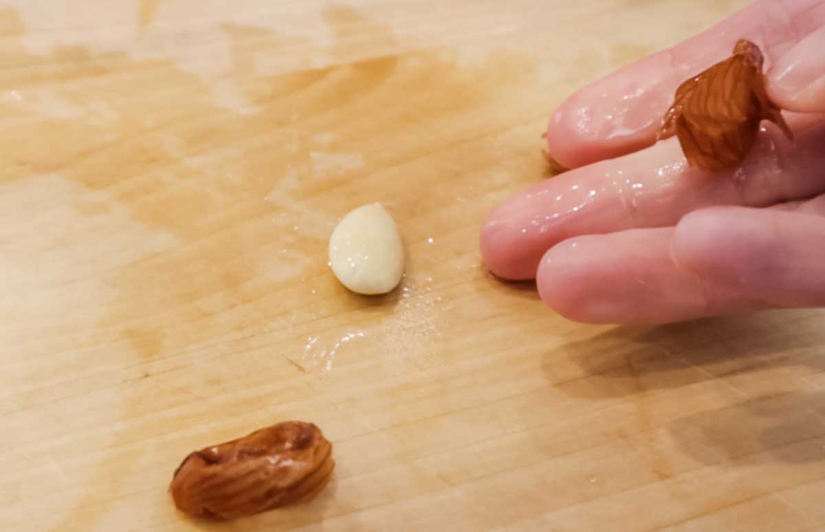 una almendra pelada, ua piel suelta y una mano mostrando la piel de una almendra