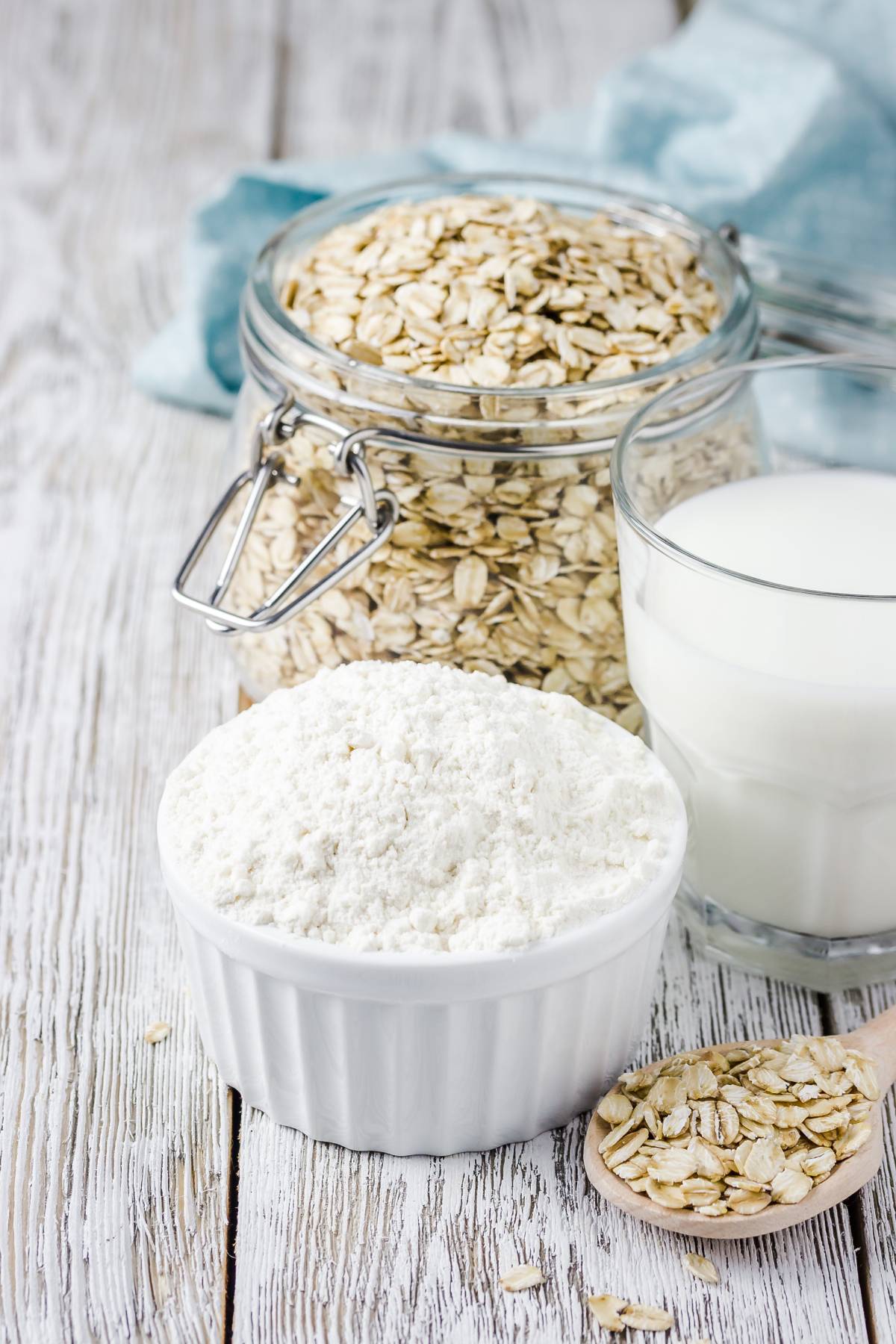 un recipiente con harina de avena, detrás un frasco con avena y un vaso con leche