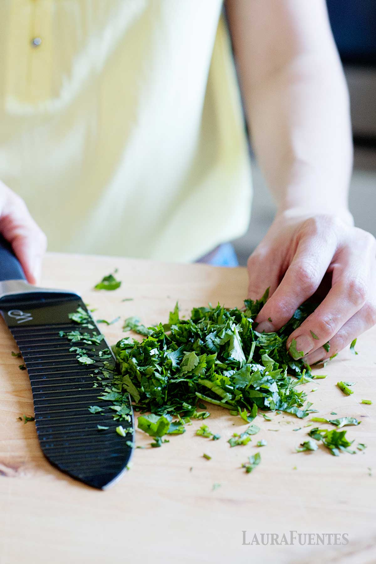 cilantro picado sobre una mesa, junto a un cuchillo y un mano