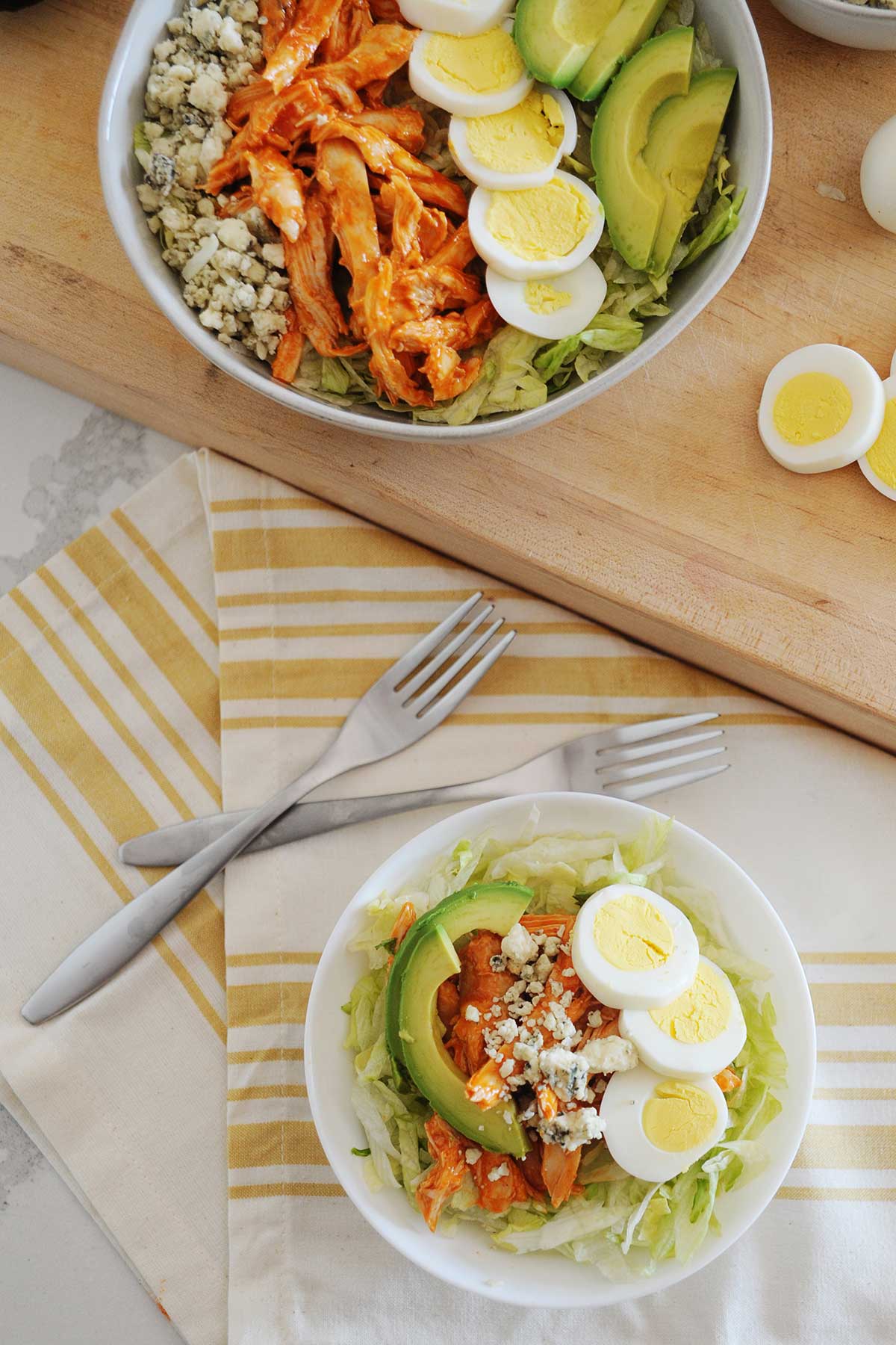 dos recipientes con ensalada de pollo Buffalo sobre una mesa, con dos tenedores y rodajas de huevo duro