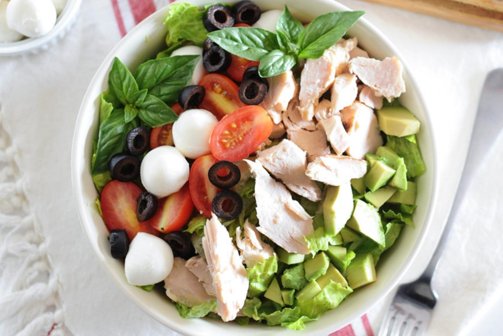 ensalada con pollo desmenuzado, tomato, aceitunas, muzzarella, aguacate y lechuga en un bol