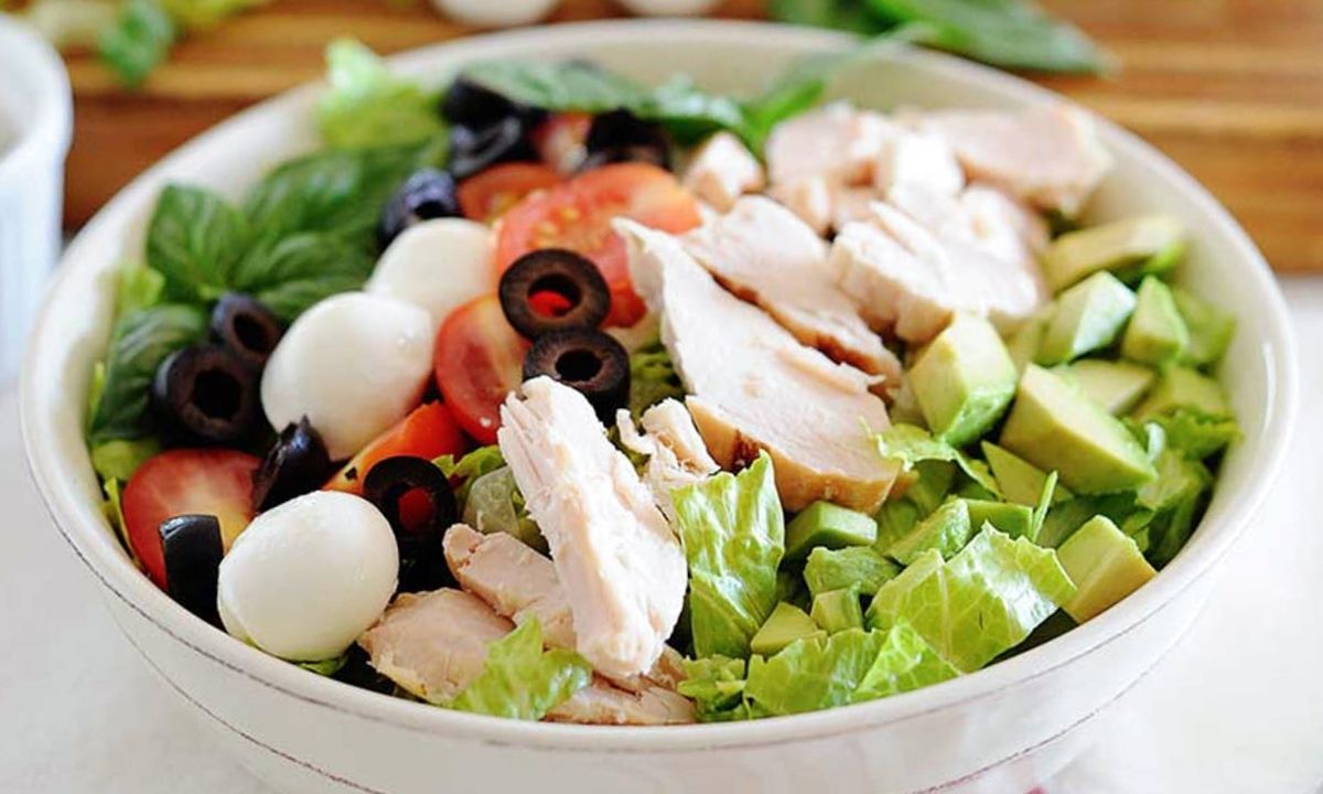 ensalada con pollo desmenuzado, tomato, aceitunas, muzzarella, aguacate y lechuga en un bol