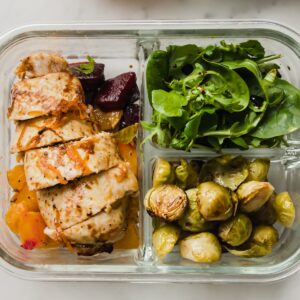 una caja de almuerzo con pollo y verduras asadas