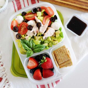 lonchera con ensalada de pollo y verduras, acompañada con frutas y crackers