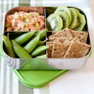 lonchera con ensalada de salmón enlatado, crackers, kiwi y verduras.