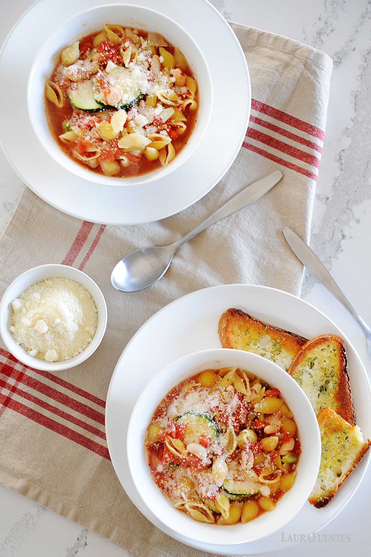 dos platos de minestrone de verduras acompañado con tostadas y queso.