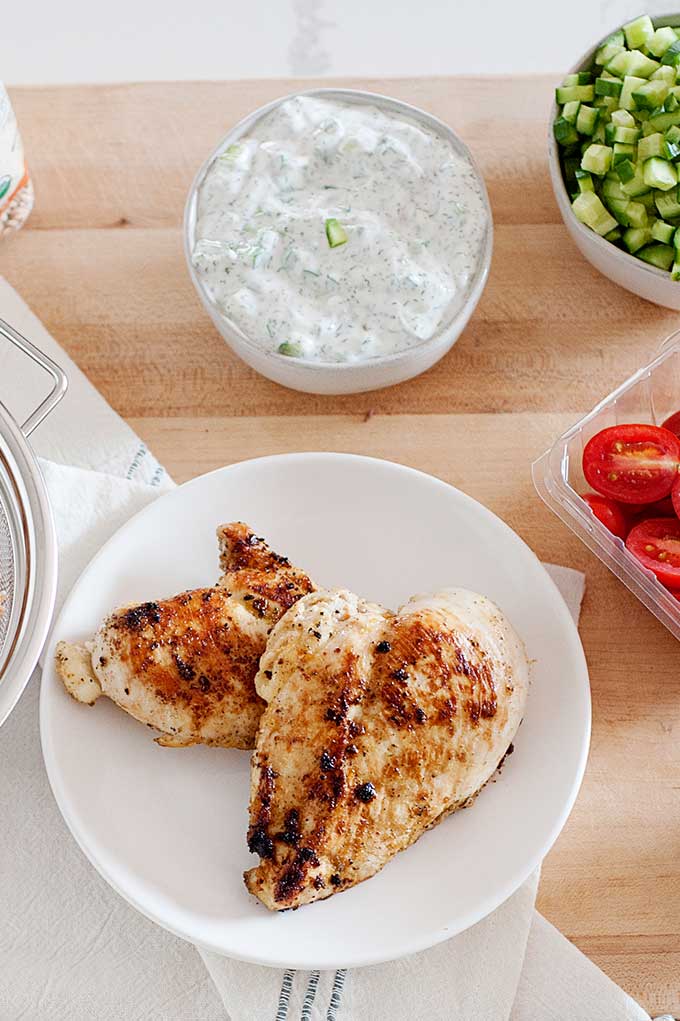 un plato con dos pechugas de pollo, un bowl con queso crema y otro con tomates