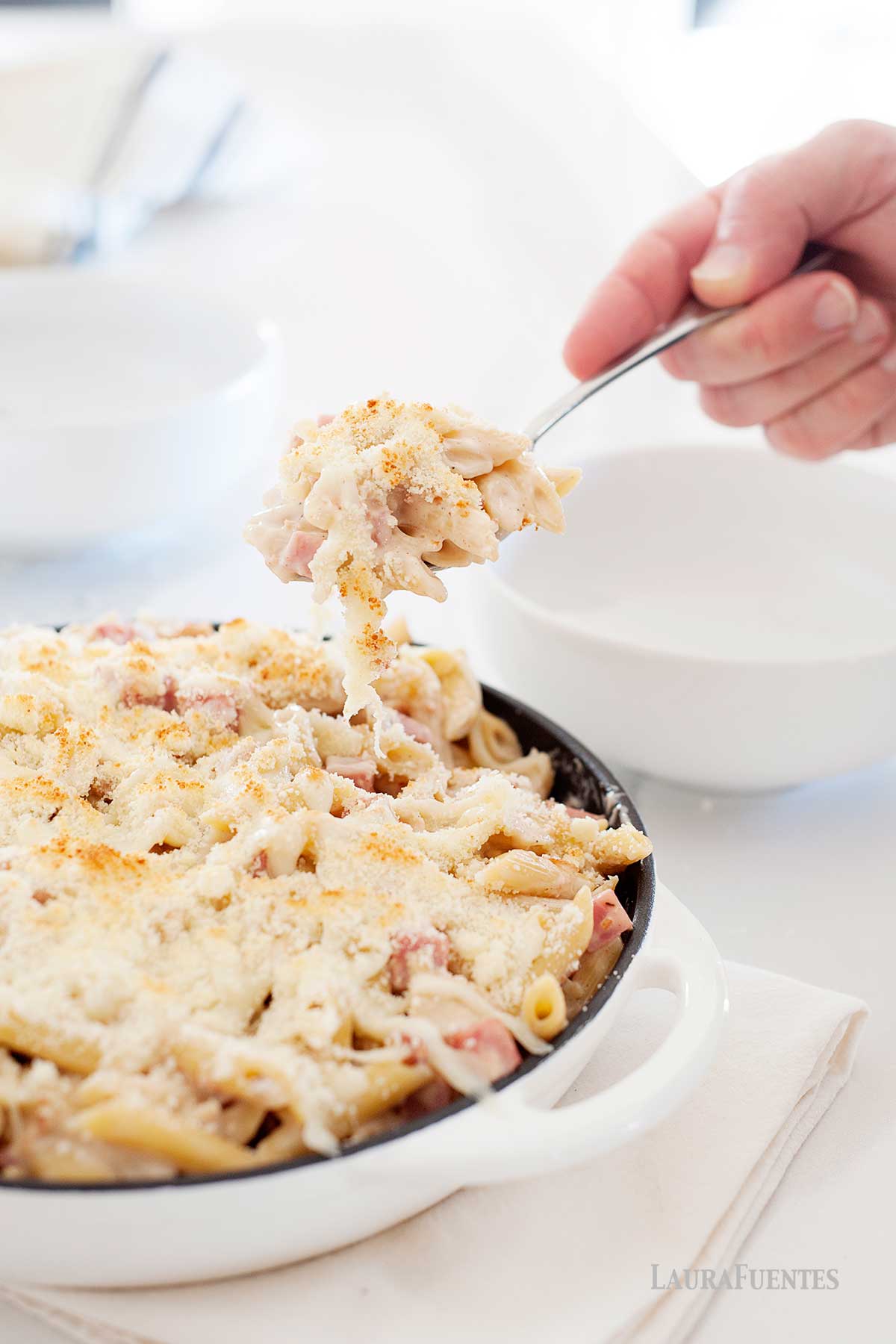 una persona sirviendo pasta con jamón y queso al horno