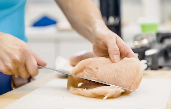 una persona mostrando cómo cortar una pechuga de pollo en filetes