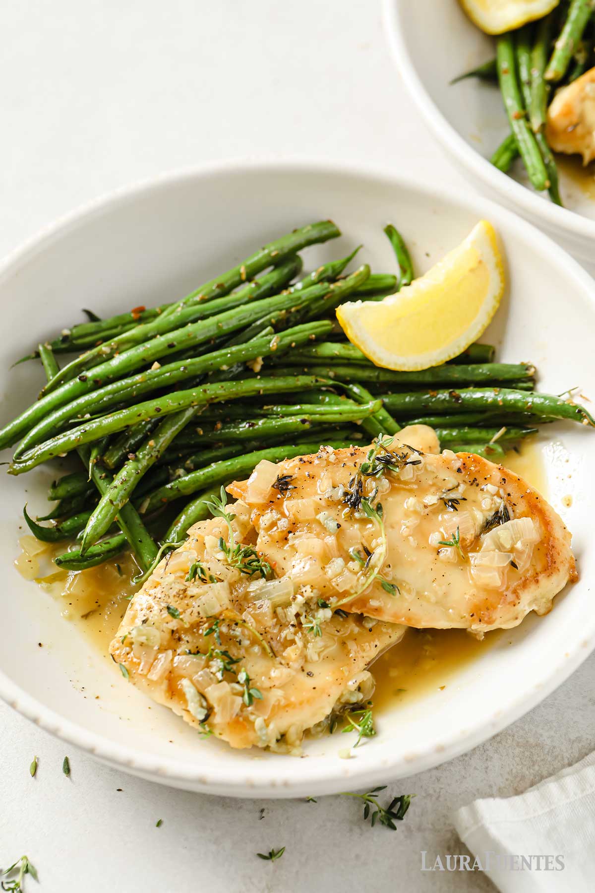 un plato con dos pechugas de pollo al vino blanco, una ración de judías verdes y un gajo de limón.