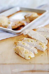 una pechuga de pollo cortada en trozos delante de una fuente con más pollo cocido.