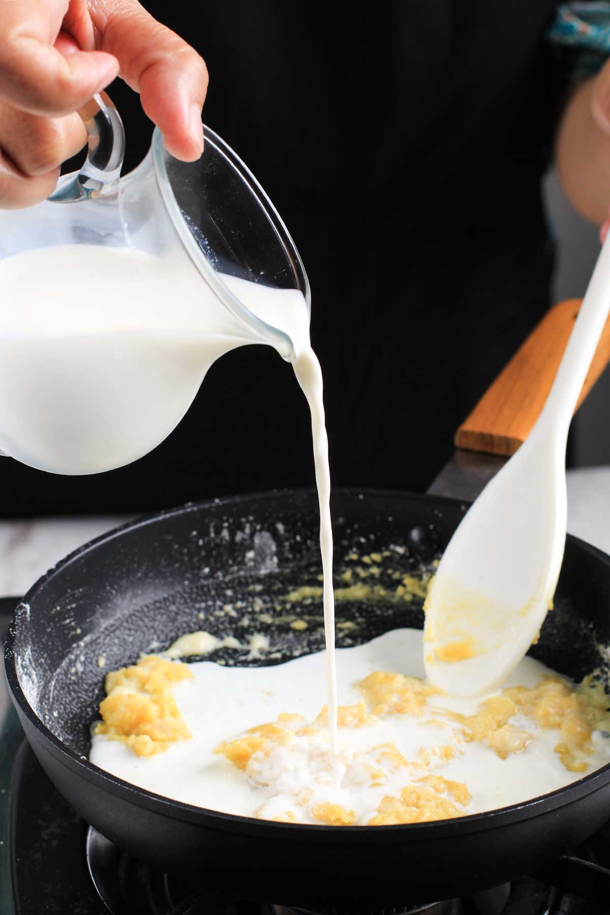 virtiendo leche dentro de una sartén haciendo salsa bechamel