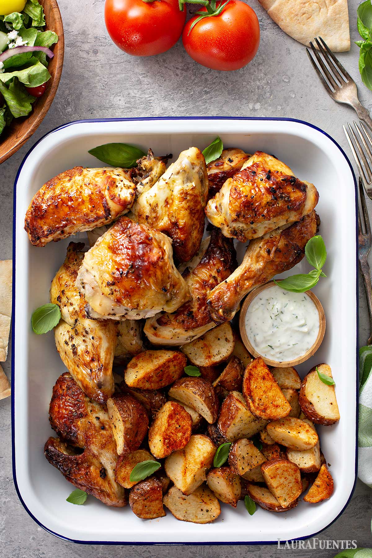 una fuente con piezas de pollo a la mostaza asadas con papas y un recipiente con aderezo.
