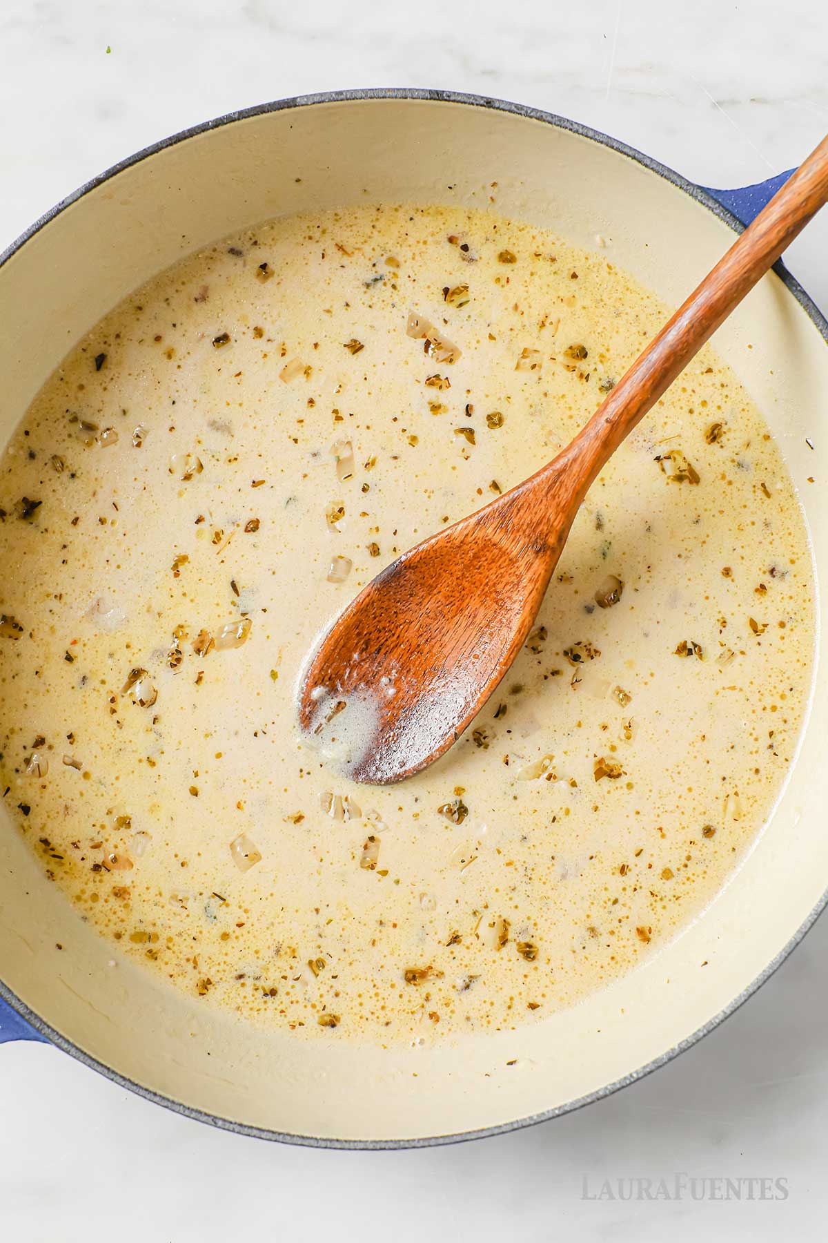 una sartén con salsa para acompañar pechugas de pollo y una cuchara de madera dentro