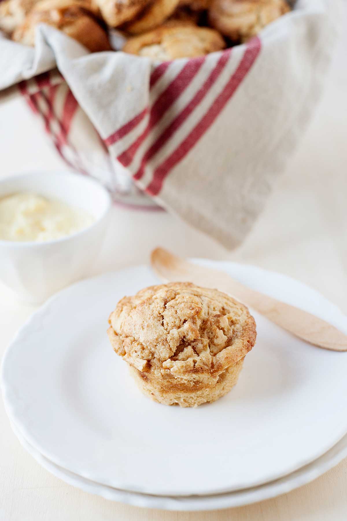 una magdalena de manzana en un plato. Detrás, una canasta con más magdalenas