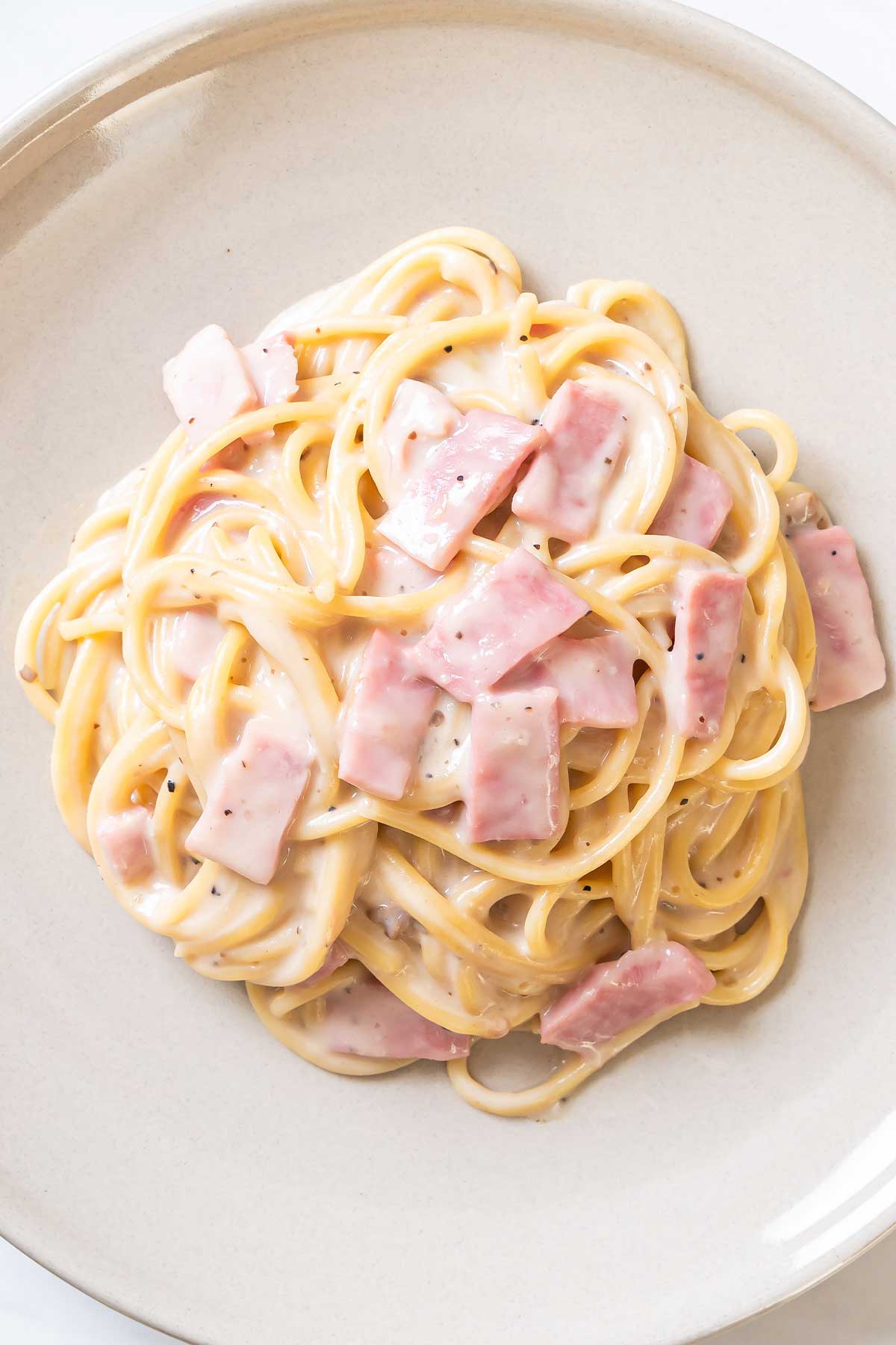 un plato de pasta con salsa alfredo con jamón