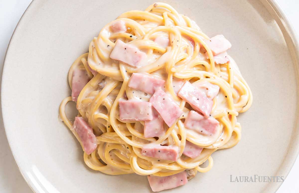 un plato de espaguetis con salsa alfredo con jamón york