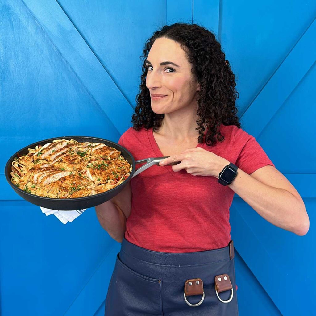Laura Fuentes holding a pan of chicken and pasta standing in front of a blue door