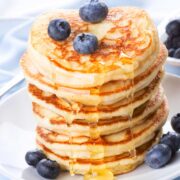 un plato con una pila de hot cakes con miel y arándanos