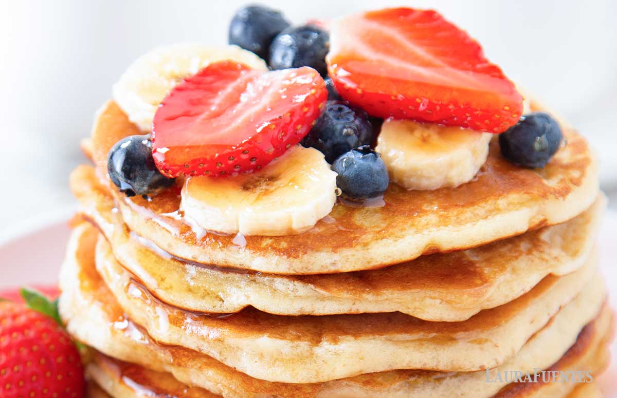 una pila de tortitas con plátano, fresas y arándanos encima